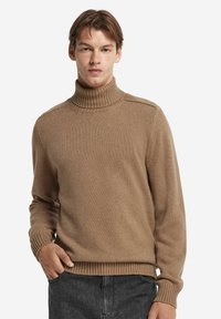 Ljusbrun polo för med ribbade manschetter och krage, tillverkad av ett mjukt, texturerat material. Enkel design, figurnära silhuett.