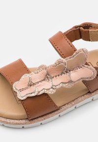 Brown leather sandal with two straps, featuring a pink and glittery butterfly embellishment across the front. White textured sole.