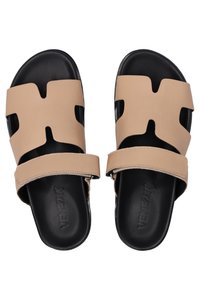 Beige leren sandalen met uitsnijdingen, zwarte rubberen zolen en een verstelbare band. Glad oppervlak met minimale details.