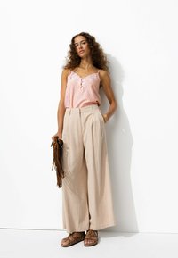 Haut sans manches rayé rose clair avec dentelle et détails de boutons, associé à un pantalon beige à jambes larges et des sandales brunes à lanières.