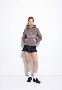 Grey hooded sweatshirt featuring "Local Heroes" in silver text, paired with a dark denim mini skirt, white socks, and black loafers.