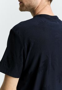 Navy katoenen t-shirt met palmboompatronen die in de stof zijn geperst. Ronde halsontwerp met korte mouwen en een relaxte pasvorm.