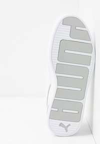 Bílé tenisky s texturovanou gumovou podešví a velkým šedým logem. Svršek má hladký povrch, doplněný jemnými švy.