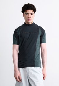 Camisa atlética de manga curta em verde escuro e preto, feita de tecido que afasta a humidade, com um colarinho alto e detalhe do logotipo refletivo.