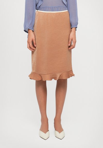 Brown knee-length skirt with textured fabric, featuring a ruffled hem. Paired with white pointed-toe heels and a light blue blouse.