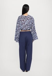 Blouse courte fluide à fleurs bleues avec manches évasées, associée à un pantalon large bleu marine. Tissu doux avec une coupe ample et un design de ceinture à l'arrière.