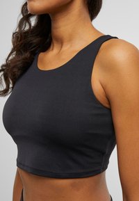 Svart avskåret tank top med rund hals, laget av glatt stoff, har brede stropper og en tettsittende silhuett. Minimale sømmer.