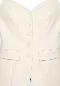 Eikonsinen bleiseri, jossa on rakenteellinen V-pääntie, kuusi kangaspäällysteistä nappia ja kaksi etutaskua; sileä, muotoiltu kangas.