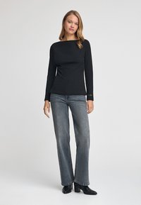 Maglietta nera a maniche lunghe con scollatura a barca, abbinata a jeans a gamba dritta blu chiaro e stivaletti neri con tacco grosso.