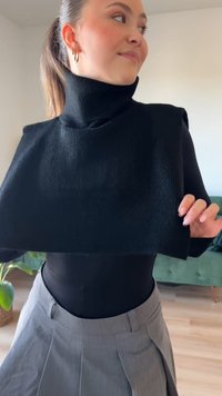 Melnā adīta augsta kakla cropped blūze ar ribotu tekstūru, kurai ir augsts apkakle un īsas piedurknes, apvienota ar pelēkiem plecu biksēm.