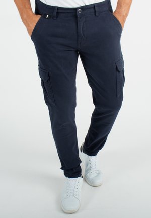 Pantalons cargo navy avec une coupe slim, en coton, dotés de deux poches latérales, de deux poches sur les cuisses et d'une fermeture éclair. Des baskets blanches viennent compléter la tenue.