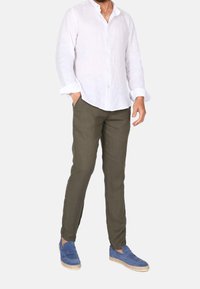 Bílá lněná košile s knoflíky, olivově zelené kalhoty a modré semišové mokasíny. Tento outfit má uvolněný střih a texturované materiály.