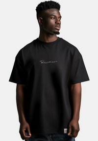 Zwart oversized t-shirt met een gladde textuur en een wit cursief logo aan de voorkant. Korte mouwen en een ronde hals.
