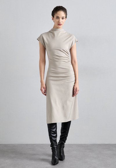 Beige aansluitende midi-jurk met korte mouwen, geplooide zijdetails, zachte textuur, gecombineerd met zwart leren laarzen tot de knie.