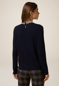 Maglione lavorato a maglia di colore blu navy con texture a coste, caratterizzato da un'apertura a chiave nel retro del collo decorata con perline decorative. Maniche lunghe, vestibilità comoda.