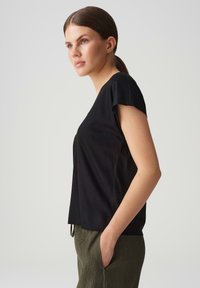 Schwarzes Kurzarm-T-Shirt mit lockerer Passform, aus weichem Stoff hergestellt, mit einem V-Ausschnitt und dezenten Nähten.