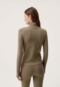 Khaki dlhý rukáv top s vysokým golierom, s rebrovanou textúrou a vertikálnymi švami, v kombinácii s priliehavými nohavicami v rovnakom odtieni.