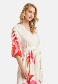 Floral dress featuring a white fabric base, vibrant red and pink patterns, loose sleeves, and a tie waist for adjustable fit.