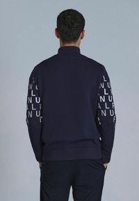 Marineblauwe sweatshirt met hoge kraag, lange mouwen en een herhaald tekstpatroon, gladde textuur en geribde tailleband.