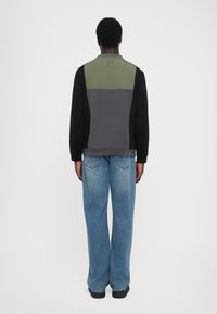 Hanorac cu blocuri de culoare, cu mâneci negre; față gri, măsliniu și verde; purtat cu blugi largi de culoare albastră; material moale, croi casual.