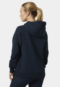 Námořnický modrý hoodie s volným střihem, dlouhými rukávy a kapucí se šňůrkou pro nastavení; vyrobeno z měkké, texturované tkaniny.