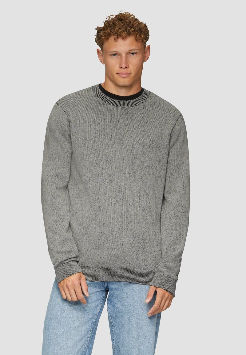 Grauer gestrickter Pullover mit einem gerippten Rundhalsausschnitt und Bündchen, der eine strukturierte Oberfläche aufweist. Getragen mit hellblauen Jeans.