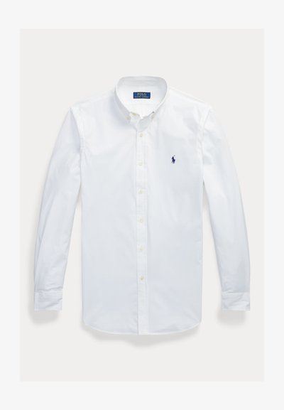 Biela dlhá košeľa na gombíky s golierom na gombíky a malým tmavomodrým vyšívaným logom na ľavej hrudi.