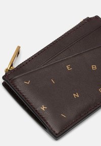 Ciemnobrązowy skórzany portfel z złotym napisem. Wyposażony w zamknięcie na zamek i teksturowaną powierzchnię z ukośnym przeszyciem. Kompaktowy i elegancki design.