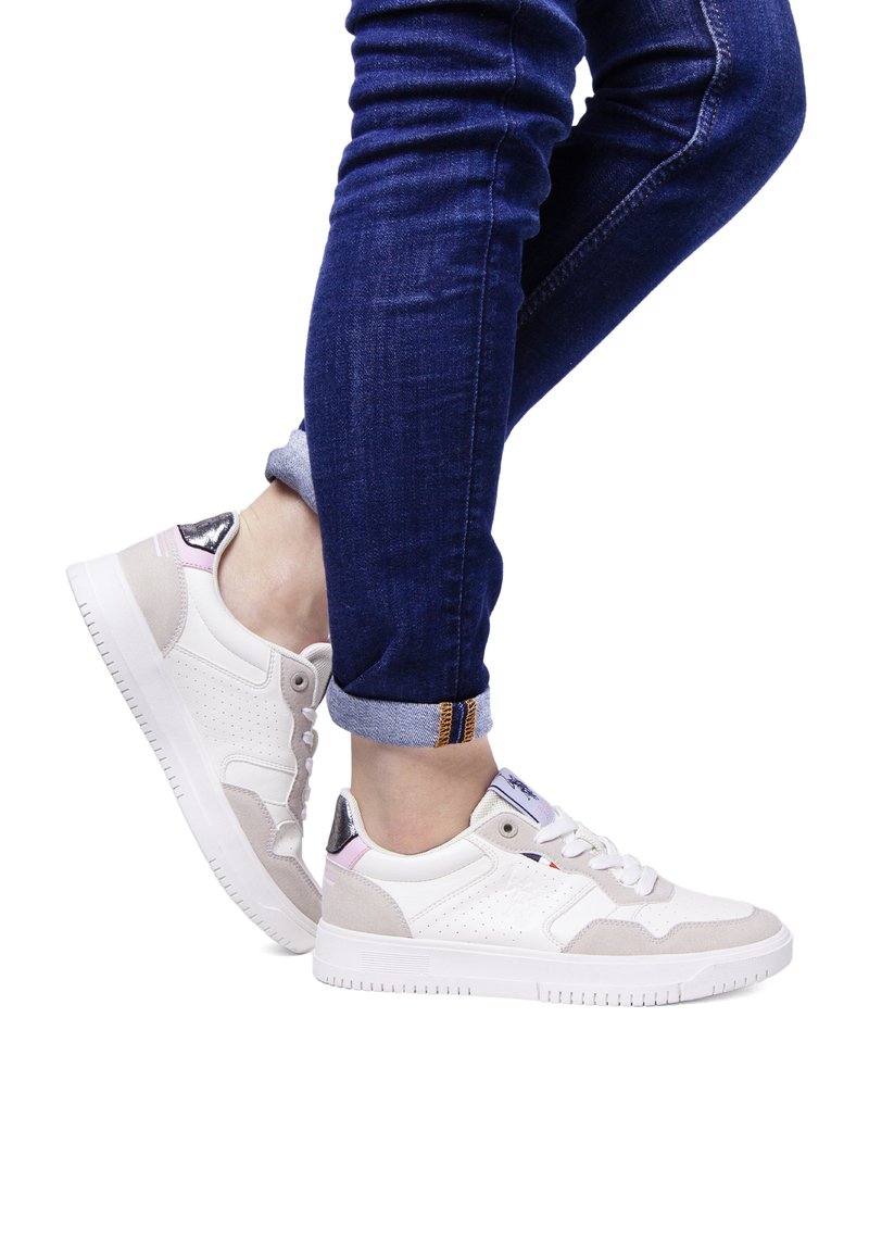 Sneaker bianchi e grigio chiaro con dettagli perforati, un tallone testurizzato e accenti pastello. Abbinati a jeans in denim arrotolati.