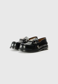 Schwarze Lederloafers mit silbernen Hardware-Akzenten, abgerundeter Zehenpartie, niedrigem Blockabsatz und dekorativen Nähten entlang der Kanten.