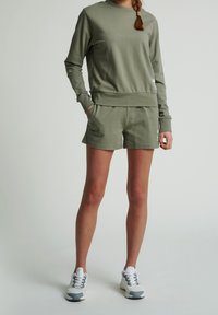Set z jemné tkaniny v olivově zelené barvě, skládající se z mikiny a kraťasů. Mikina má kulatý výstřih a dlouhé rukávy; kraťasy mají boční kapsy a elastický pas.