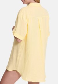 Geel overhemd met knoopsluiting in een lichtgewicht stof. Heeft een relaxte pasvorm, korte mouwen en een rugpand met plooidetail.