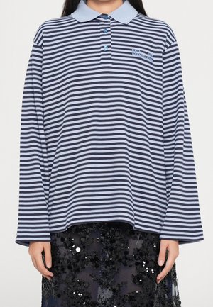 Person wearing a long-sleeve navy and light blue striped polo shirt with a ribbed collar and black sequined skirt.