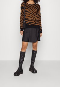 Maglione a righe marroni e nere, gonna in raso nero, stivali neri con plateau al ginocchio e una piccola borsa nera a tracolla.