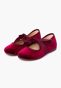 Bailarinas de terciopelo burdeos con punta redondeada, tira elástica con detalle de lazo y suela plana de goma. Sin patrones ni acentos visibles.