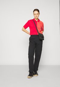 Rode cropped polo shirt met korte mouwen, zwarte cargo broek met zijzakken en zwarte sneakers met een lichte zool en textuurdesign.