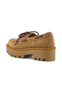 Chaussure en daim tan avec une semelle épaisse et robuste. Présente des lacets marron contrastants à travers des œillets en ton or et un détail de couture texturé sur le côté.