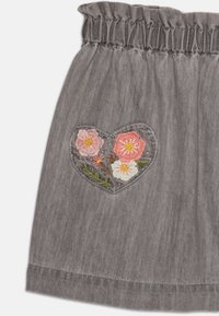 Grå skjørt med elastisk liv, som har et hjerteformet broderipatch med rosa og hvite blomster og grønne detaljer på et teksturert stoff.
