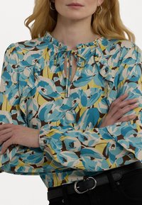 Halenka s dlouhým rukávem, zdobená květinovým vzorem v odstínech modré a žluté, s volánkovým výstřihem a vázáním v přední části.
