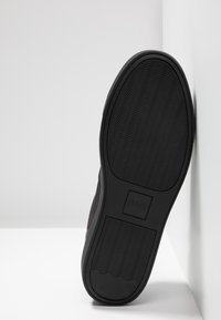 Czarny sneaker z teksturowaną gumową podeszwą, posiadający falisty wzór i detal z logo. Zewnętrzna część ma gładkie wykończenie tekstylne i subtelne akcenty.