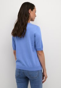 Lichtblauwe trui met korte mouwen van zacht materiaal, met een ronde halslijn en geribbelde zoom, gecombineerd met spijkerbroek.