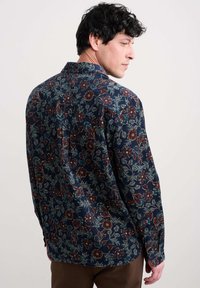 Ziedu raksta krekls ar tumši zilu fona krāsu, garām piedurknēm un klasisku apkakli. Materiāls izskatās teksturēts ar maigu spīdumu.