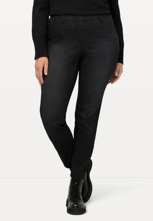 Mustat farkut slim fit -leikkauksella, elastisella vyötäröllä ja huomaamattomilla ompeluyksityiskohdilla, yhdistettynä mustiin nauhakorollisiin saappaisiin.