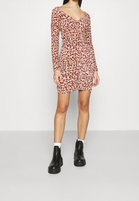 Vestido ajustado de manga larga con un patrón floral en rojo y rosa, escote en V y detalles fruncidos. Combinado con botas negras de tobillo.