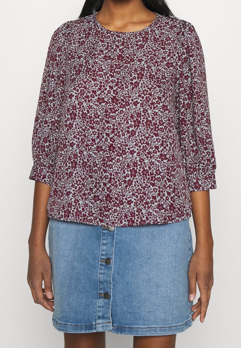 Femme portant un haut à manches longues à fleurs violettes et une jupe en jean bleu clair avec des boutons sur le devant.