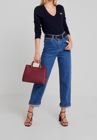 Red leather handbag with tan handles, paired with a black V-neck sweater and high-waisted blue denim jeans, showcasing a casual look.