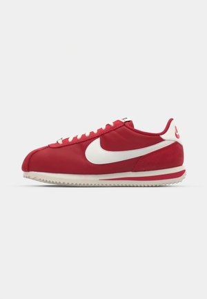 Červené tenisky Nike s bielym swooshom, vyrobené z hladkej textílie a semišu, s plochými bielymi šnúrkami a drsnou gumovou podrážkou.