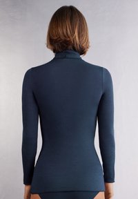 Top s dlouhým rukávem a rolákem v tmavě modré barvě, který má přiléhavý střih a hladkou texturu, vysoký límec a bezešvou zadní část.