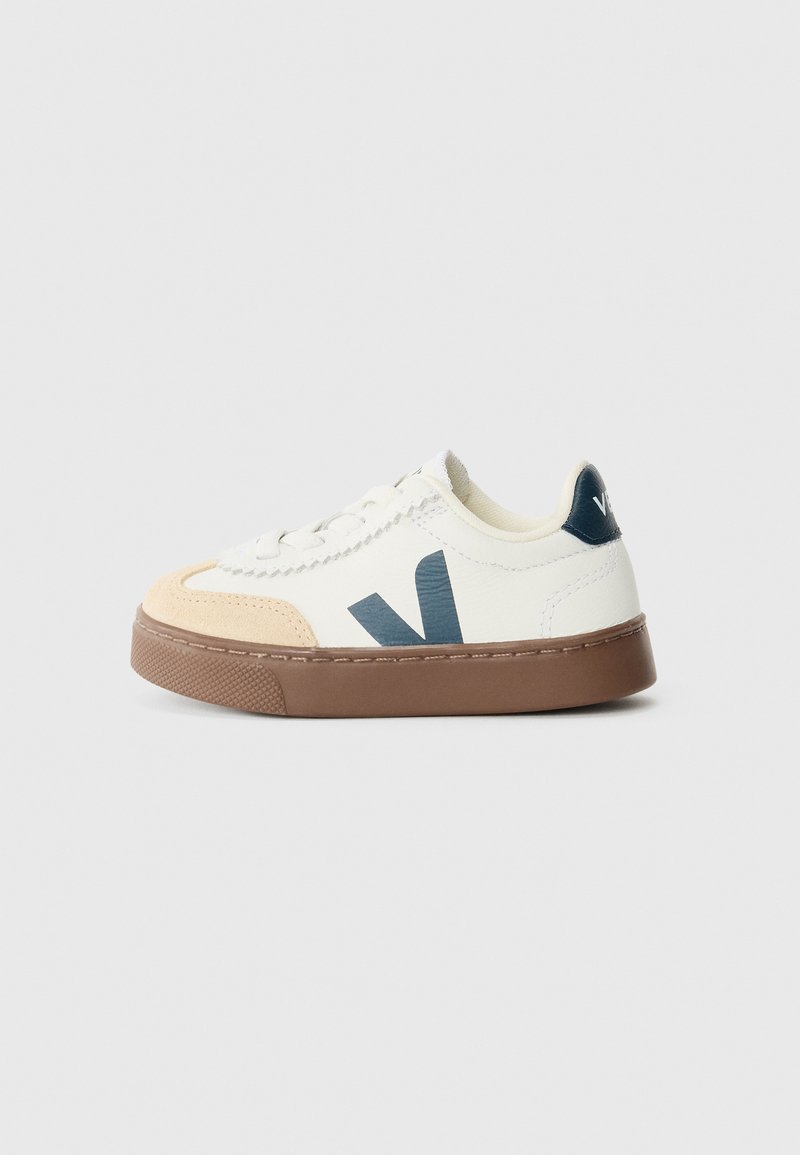 Sapatilhas com um cabedal em couro branco, detalhes em suede bege claro, logotipo azul escuro e sola de borracha castanha. Design com atacadores e detalhes texturizados.