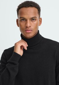 Schwarzer Rollkragenpullover aus weichem Material, mit geripptem Kragen und Bündchen, tailliert geschnitten und mit glatter Textur.